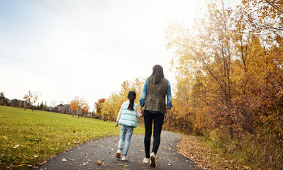 Obraz premium Mom, back and holding hands with child for walk, bonding or outdoor adventure on journey in nature. Rear view of mother strolling with daughter, kid or little girl for sidewalk, autumn season or park