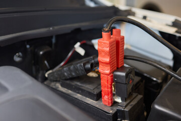 Closeup photo of black car battery connected with jumper cables for repair or recharging