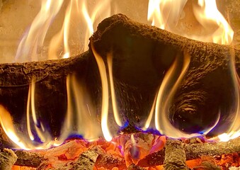 A burning log in an indoor fireplace with hot coals around it