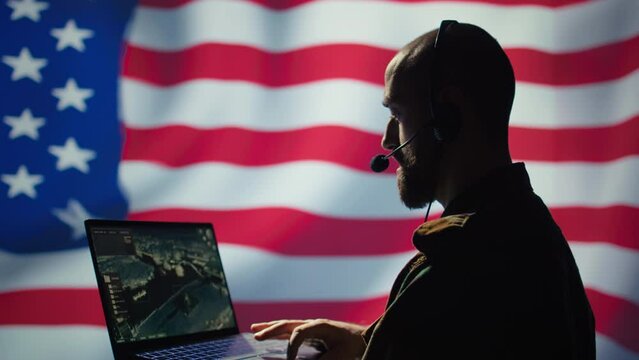 US Air Force dispatcher looking at surveillance transmission on device, relaying data to ground soldiers from control room using headset, isolated over United States flag background, camera B