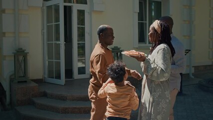 Full shot of young African American man arriving to visit father with wife and son, black boy running to hug grandfather on porch by front door, everybody embracing and greeting each other - Powered by Adobe