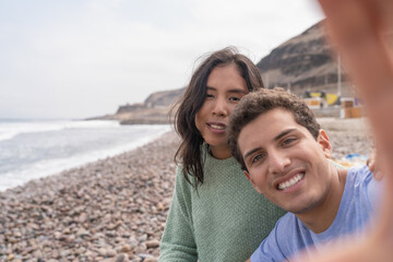 Obraz premium Latin young couple taking a selfie sitting on a beach