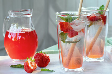 Summer refreshing homemade cocktail with strawberries and mint on the table in a bright summer kitchen in the garden