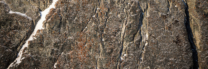 Rock texture. Snow and cracks on the surface of the cliff. Natural stone background.