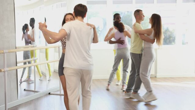 Slim young man and woman practicing waltz dance in training hall during group dancing classes