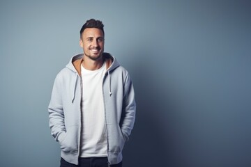 Portrait of a handsome young man wearing a hoodie and smiling while standing against grey background