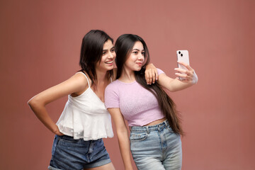 Two Female Friends Are Clicking Photos While Standing Over A Pink Background