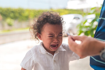 A young asian boy with curly hair crying and throwing a tantrum after not getting his toy back.