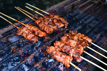 Satay is being grilled on a grill using coals and emitting smoke