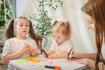 Young mother or babysitter, little daughter, sister teenager girl drawing at table in room. Painting, doing homework, family enjoying leisure at home