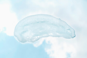 Smear of facial cleansing foam against background of blue sky and clouds.