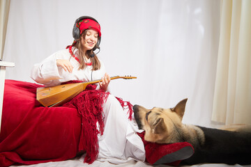 A girl in red scarf, white shirt, with shawl and balalaika in black sunglasses with a shepherd dog....