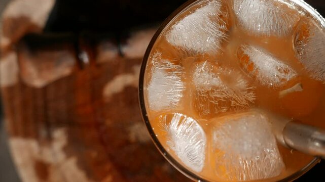 POV of a person mixing a Caipirinha on a sunny table. A wooden muddler next to a Caipirinha glass. Someone stirring a Caipirinha cocktail with a drinking straw. A close-up of a Brazilian Caipirinha.