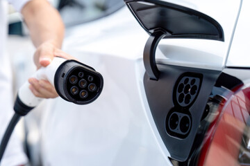 Hand insert EV charger plug into electric vehicle to recharge EV car battery from outdoor charging...