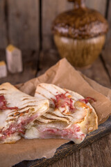 Quesadilla with cheese and ham on craft paper on a wooden table