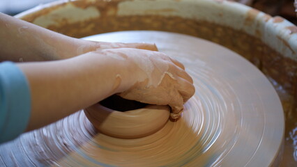 Kid hands playing with clay on throwing wheel.