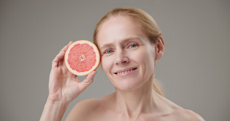 Real people - concept of age, beauty, health and dry skin care - beautiful mature Caucasian middle aged woman in her 50s holding half a grapefruit as a source of vitamins and nutrients