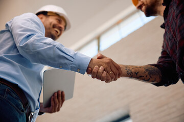 Close up of building contractor shaking hands with worker at construction site.