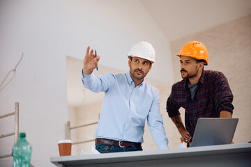 Building contractor and worker analyzing housing plans at construction site.