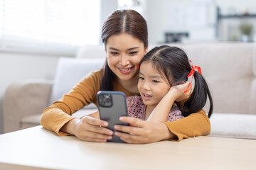 image of mother and daughter cuddling on the sofa using mobile phone waching movie online,