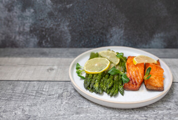 Baked salmon and asparagus with salad and lemon on dark background. Top view. 