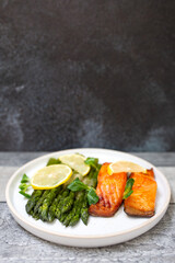 Baked salmon and asparagus with salad and lemon on dark background. Top view. 