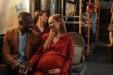 Pregnant couple smiling and holding hands on a bus