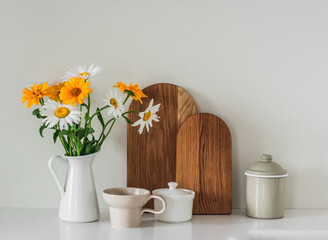 Kitchen still life - a jug with flowers, cutting boards, dishes on a light kitchen surface