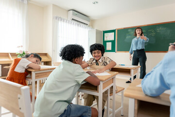 Diversity student talking to each other while teacher teach in classroom.