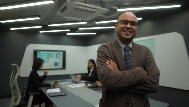 Portrait of young motivated leader asian business man standing with crossing his arms and looking at camera in meeting room, startup entrepreneur with background of partnership meeting in office room.
