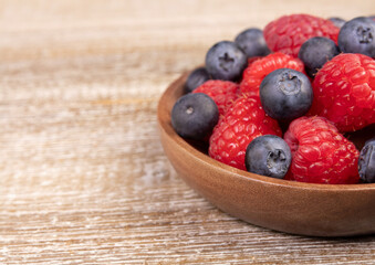 Mix of blueberries and raspberries in wooden plate on a rustic table.