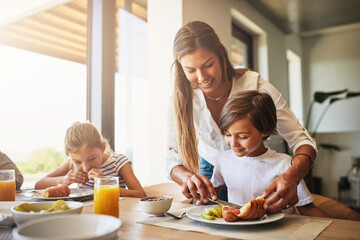 Family, breakfast and help in house with cereal, juice and fruit for health or nutrition by table. Woman, knife and kid together in home with food for wellness, brunch and bonding with mom in morning