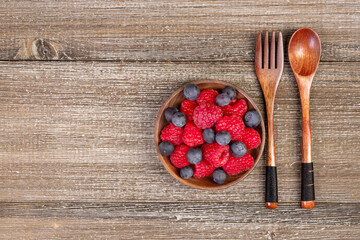 Mix of blueberries and raspberries in a plate with wooden fork and spoon.