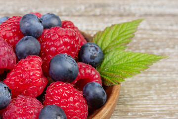 Plate with raspberries and blueberries with leaves on the wooden rustic table.