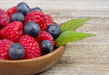 Plate with raspberries and blueberries with leaves on the wooden rustic table.