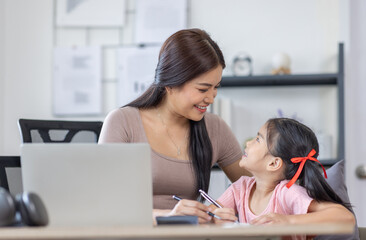 Asian business lady working on computer while her daughter hugging her