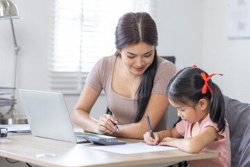 Obraz premium Asian business lady working on computer while her daughter hugging her