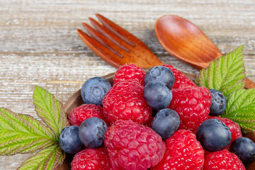 Mix of blueberries and raspberries in a plate with wooden fork and spoon.