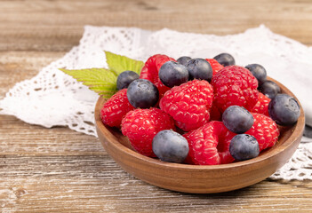 Plate with raspberries and blueberries on the wooden table with laced cloth.
