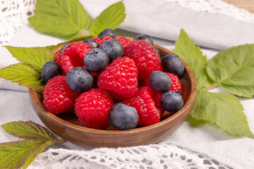 Plate with raspberries and blueberries on the wooden table with laced cloth.