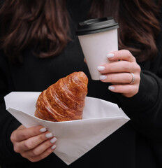 Woman holding coffee and croissant outdoors