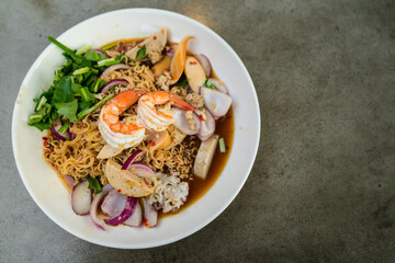 Spicy mixed seafood salad with noodle in white plate at restaurant. Thai street food classic, Yum Mama, or Thai spicy and tangy instant noodle salad.