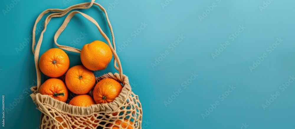 Poster top view flat lay composition featuring a beige string bag filled with oranges on a blue background,