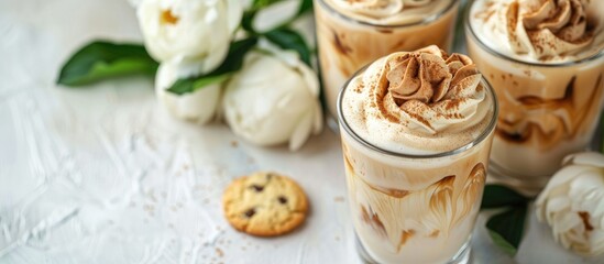 Korean trend, Dalgona Coffee with milk and ice, a cold drink with whipped brown cream in a glass on a white table with cookies and peonies, in a top view copy space image.