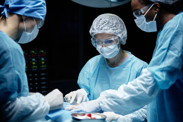 Waist up portrait of medical team with female surgeon performing operation in blue light at...