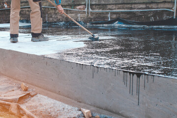 Worker Applying Black Waterproofing Material to Concrete Foundation