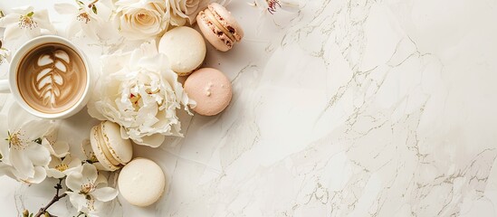 A delicate bouquet of pastel beige flowers, along with macarons and coffee, elegantly arranged on a white marble surface with copy space image.