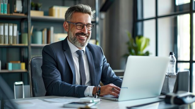 Smiling mature adult business man executive sitting at desk using laptop. Happy busy professional mid aged businessman ceo manager working on computer corporate technology in office