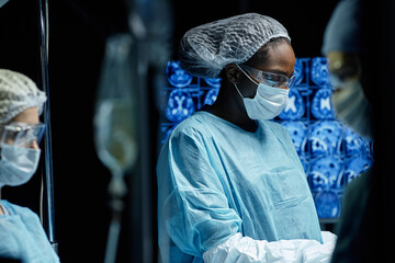 Side view portrait of African American woman as female surgeon wearing full protective clothing in operation with screens and monitors in background copy space