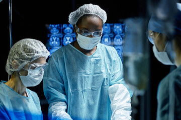 Waist up portrait of African American woman assisting in operation at hospital wearing mask and...